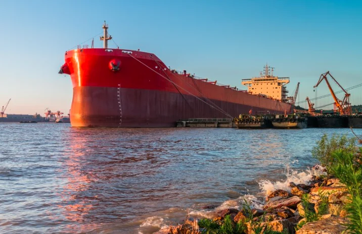 Large red-hulled vessel moored at a river port